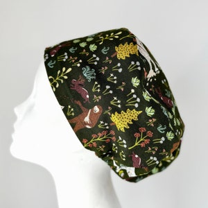 May include: A green scrub hat with a woodland animal print featuring sloths, deer, and rabbits. The hat has a dark green background with colorful animals and foliage.
