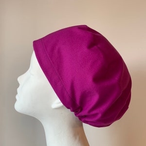 May include: A magenta scrub hat made of soft fabric. The hat has a gathered elastic band at the back.