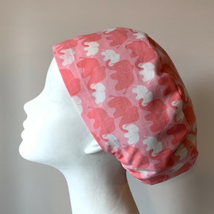 May include: A pink scrub hat with a white elephant print. The hat is made of a soft, comfortable fabric and is ideal for nurses, doctors, and other healthcare professionals.