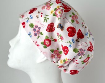 May include: A white scrub hat with a pink floral pattern and red hearts. The hat has the words "I love you" and "so very" printed on it.