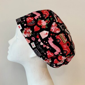 May include: Black scrub hat with a Valentine's Day print featuring red trucks, hearts, flowers, and the text "Falling in Love".