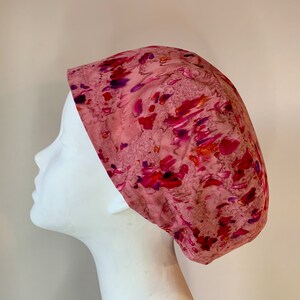 May include: A pink surgical scrub hat with a colourful abstract pattern in shades of pink, purple, and orange.