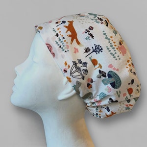 May include: A white scrub hat with a colorful woodland print featuring foxes, mushrooms, and leaves.