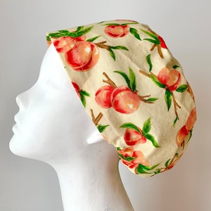 May include: A white scrub hat with a peach print. The hat has a gathered back and a tie at the back.