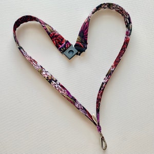 May include: A floral patterned lanyard with a black plastic clip and a silver swivel hook. The lanyard is shaped like a heart.