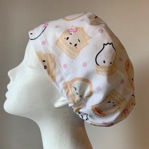 May include: White scrub hat with a pink and brown cartoon print of steamed buns and dumplings. The hat has a gathered elastic band at the back.