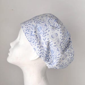 May include: A white and blue patterned surgical scrub cap with a floral design. The cap is made of a soft, breathable fabric and is designed to be comfortable to wear.