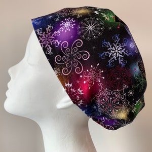 Könnte beinhalten: Eine schwarze OP-Mütze mit einem farbenfrohen Ombre-Design mit weißen Schneeflocken und Spiralen. Die Mütze ist aus einem weichen, bequemen Stoff gefertigt und perfekt für medizinisches Personal.