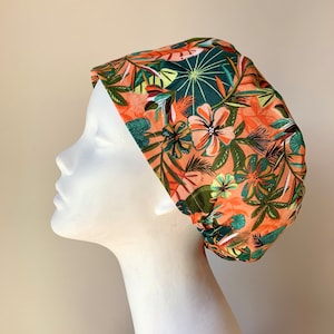 May include: A surgical scrub cap with a tropical print featuring orange, green and brown colours. The cap has a floral pattern with leaves and flowers.