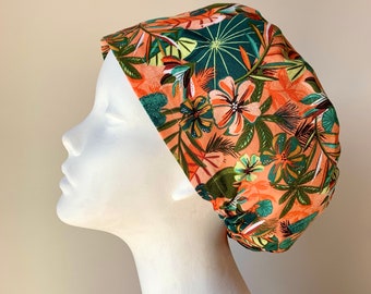 May include: A surgical scrub cap with a tropical print featuring orange, green, and brown colors. The cap has a floral pattern with leaves and flowers.