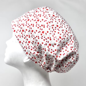 May include: A white medical scrub cap with a repeating pattern of red crosses and gray medical symbols. The cap is designed to cover the head and hair, commonly used in healthcare settings.
