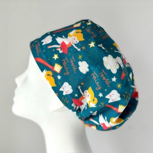 May include: Teal blue scrub hat with a whimsical pattern of tooth fairies, toothbrushes, stars, and clouds. The text "Tooth Fairy" is repeated throughout the pattern.