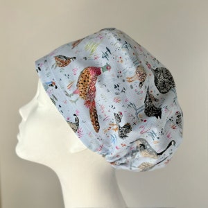 May include: A light blue scrub hat with a colourful pattern of various birds, including a pheasant, quail, and other birds. The hat has a gathered elastic band at the back.