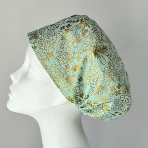 May include: A light blue scrub cap with a gold floral pattern. The cap is made of a soft, comfortable fabric and is perfect for healthcare professionals.