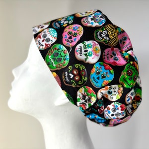 May include: Black scrub hat with a colorful sugar skull pattern. The skulls are decorated with flowers and other details.