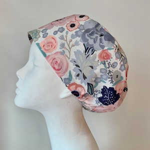 May include: A white scrub cap with a floral print featuring pink, blue, and green flowers. The cap has a tie at the back.