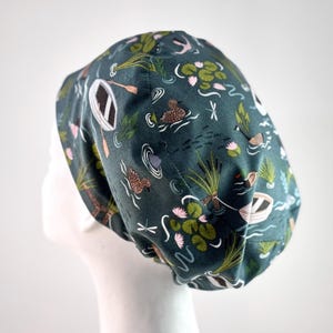 May include: A green scrub hat with a pattern of ducks, boats, and lily pads.