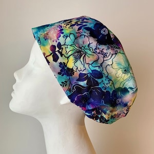 May include: A blue and white floral print scrub hat with a tie at the back. The hat has a colorful floral pattern with a blue background.