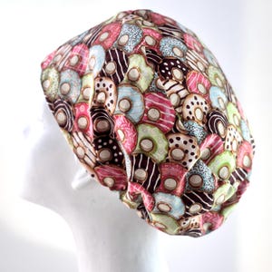 Könnte beinhalten: Eine braune, rosa, grüne und blaue gemusterte OP-Mütze mit Donut-Design.