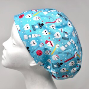 May include: A light blue surgical scrub cap with a repeating pattern of smiling teeth, toothbrushes, toothpaste tubes, and dental floss picks. The cap is designed for medical professionals.