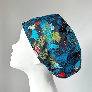 May include: A dark blue scrub hat with a colourful floral and nature-inspired print. The print features flowers, leaves, and snails.