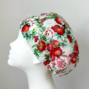 May include: A white scrub hat with a red pomegranate print. The hat has a gathered elastic band at the back.