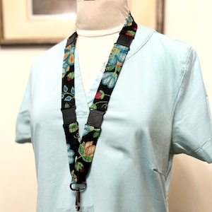 Peut inclure: Un cordon noir et bleu à motif floral avec un porte-badge en plastique transparent. Le cordon est doté d'une fermeture à pression noire et d'un crochet en métal argenté.