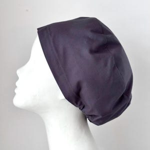 May include: A dark gray scrub cap made of fabric. The cap is gathered at the back and has a seam around the edge.