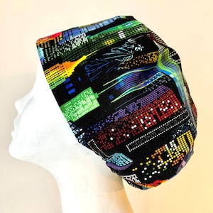 May include: A black scrub hat with a colourful pixelated city skyline design. The hat has a bright green, blue, red, yellow, and purple colour scheme.