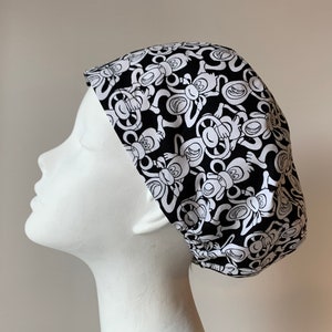 May include: Black and white scrub hat with a pattern of monkeys. The monkeys are all facing forward and have a playful expression.