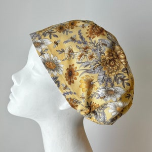 May include: A yellow floral scrub hat with a pattern of white and brown flowers, bees, and leaves.
