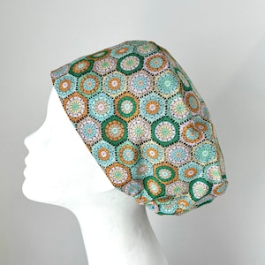 May include: A green, blue, orange, and white patterned scrub hat with a geometric design. The hat is made of fabric and has a rounded shape.