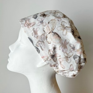 May include: A white scrub cap with a brown and pink butterfly print. The cap has a tie at the back.