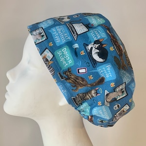 May include: A blue scrub hat featuring a pattern of cats and squirrels using laptops and phones. The text on the hat includes "Caaaa TttUd", "Dogs R Stupet", "Pprer rrrfe ctii", "ccccAtT bButtttt sryt999", "napp///", "AShT", "STY", and "dmessage Sert".