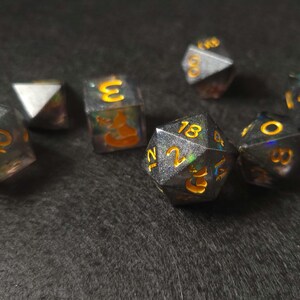 May include: A set of six iridescent dice with black and gold numbers. The dice are made of a translucent material that shimmers in the light.
