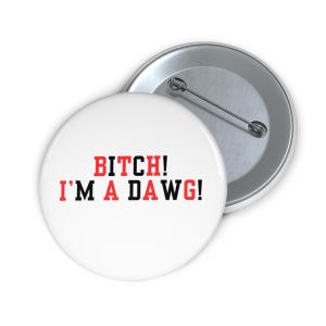 Peut inclure: Bouton blanc avec le texte "BITCH! I'M A DAWG!" en rouge et noir. Le bouton est rond et possède une épingle métallique au dos. Un autre bouton est visible en arrière-plan.
