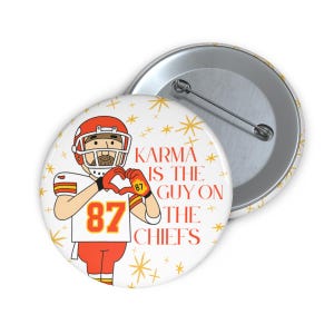 Puede incluir: Un botón blanco con un jugador de fútbol americano de dibujos animados con casco y uniforme rojos, formando un corazón con las manos. El texto "Karma is the Guy on the Chiefs" y el número 87 están impresos. Se ve un segundo botón.