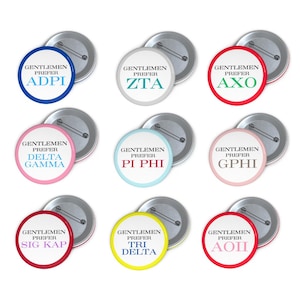 Puede incluir: Una colección de botones redondos con la frase "GENTLEMEN PREFER" sobre letras griegas. Los botones tienen varios esquemas de color, incluyendo azul, verde, rojo, rosa y amarillo, con respaldos de metal plateado.