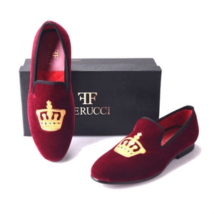 May include: A pair of burgundy velvet loafers with a gold crown embroidered on the top. The loafers have a black sole and are made by the brand "TF Ferrucci".
