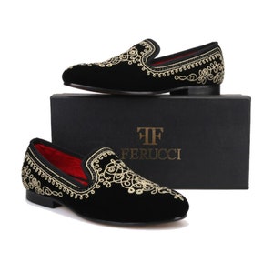 Puede incluir: Zapatos de vestir de terciopelo negro con diseños florales bordados en dorado. Los zapatos están sobre una caja negra con el texto "TF Ferrucci" en la parte delantera.