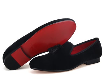 Op de afbeelding: Zwarte fluwelen loafers met een kwast detail en een rode leren zool.