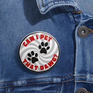 May include: A round button with the text "CAN I PET THAT DAWG?" in red, with black paw prints on a gray and white swirl design. The button is set against a denim jacket.