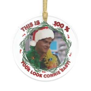 Conrad Fisher wearing a colorful feather boa and xmas lights along his neck he has a Santa hat on his head HIs image is from the scene where Belly tells him this is 100 precent your look connie Baby image outlined by a green wreath Text is in red