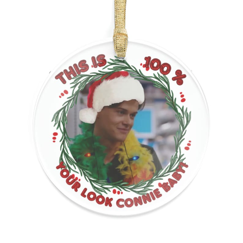 Conrad Fisher wearing a colorful feather boa and xmas lights along his neck he has a Santa hat on his head HIs image is from the scene where Belly tells him this is 100 precent your look connie Baby image outlined by a green wreath Text is in red