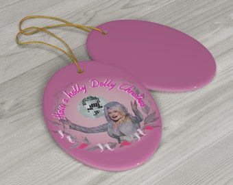 Könnte beinhalten: Rosaer ovaler Weihnachtsbaumschmuck aus Keramik mit einem Porträt von Dolly Parton, die eine Discokugel hält, mit dem Text "Have a Holly Dolly Christmas".