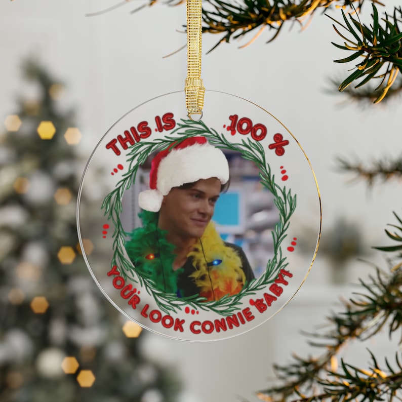 transparent acrylic glass ornament shaped as a circle & hung by a gold, sparkly ribbon. design is fictional character Conrad Fisher from The Summer I turned pretty. He is wearing a Santa hat.  christmas lights on  his neck along with a feather boa