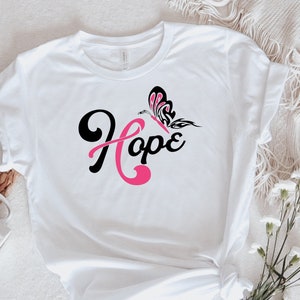 May include: White t-shirt with a pink ribbon and butterfly design. The text "Hope" is written in black cursive.