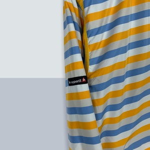 May include: A blue and yellow striped long-sleeved jacket with the logo "le coq sportif" on the left sleeve.