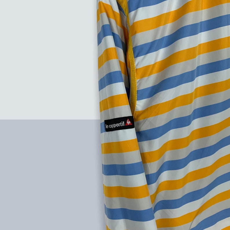 May include: A blue and yellow striped long-sleeved jacket with the logo "le coq sportif" on the left sleeve.
