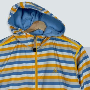 May include: A blue and yellow striped hooded jacket with a zipper closure. The jacket has a logo of a triangle with a rooster inside on the left side of the chest.
